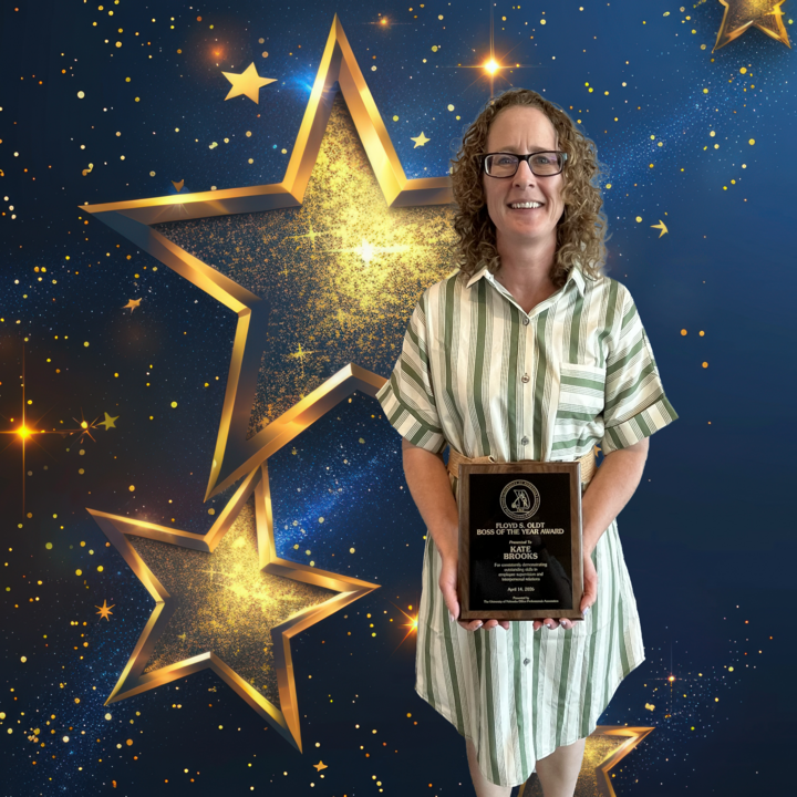 Woman in green-striped dress holding a plaque, standing against a blue and gold starry backdrop.